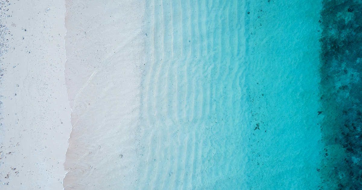 Aerial view from a beach showing a gradient colour from the sand to the bluish water 