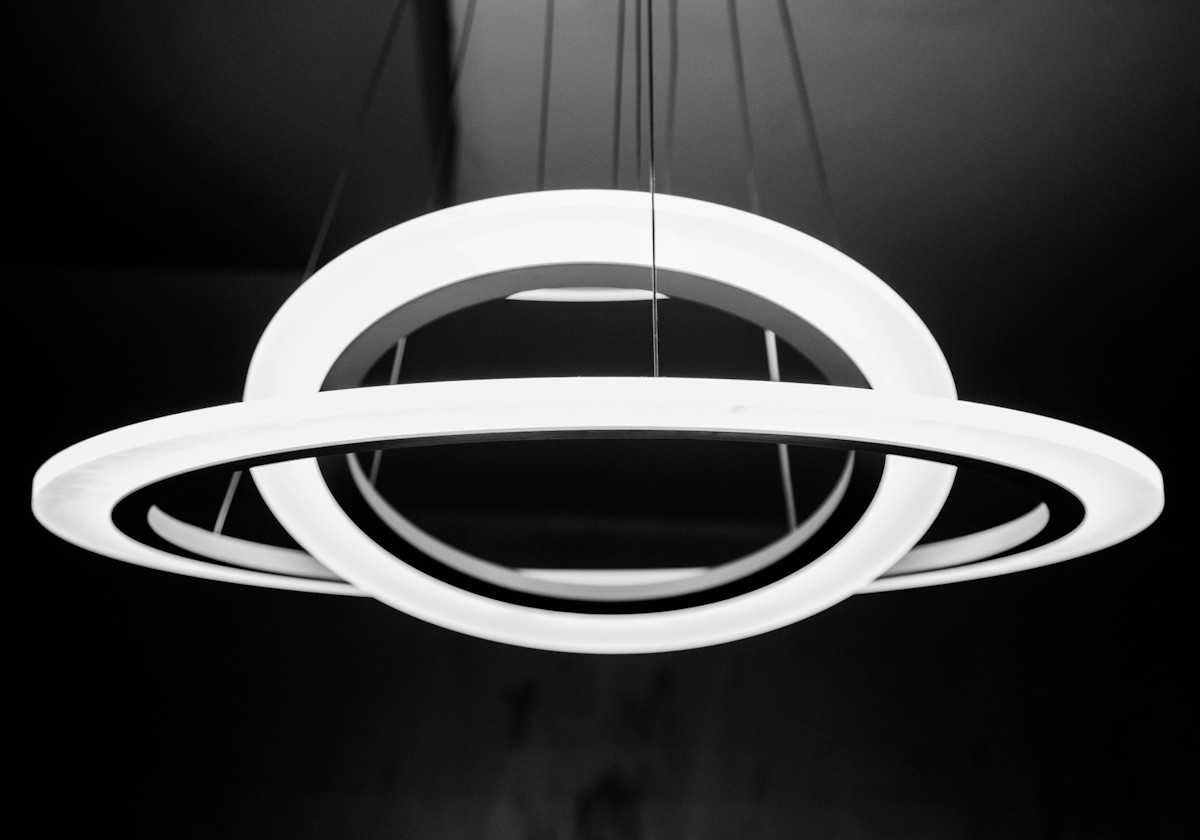 A large horizontal white flat sided hoop hanging with a second smaller hoop hanging inside it at an angle, against a dark background.
